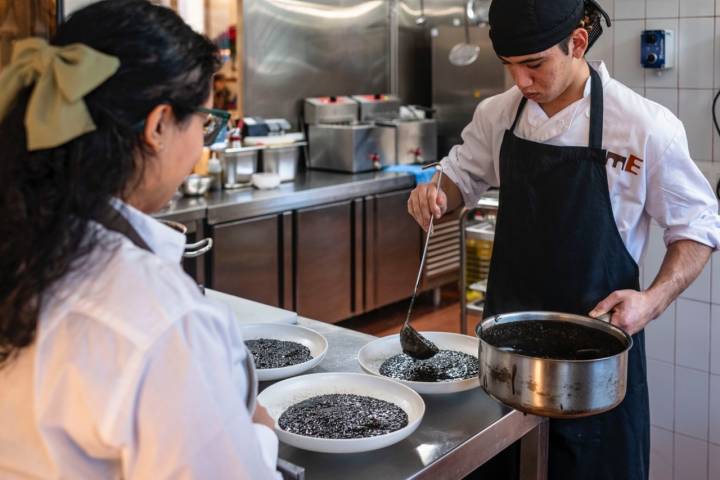 Dos trabajadores en una cocina sirviendo lentejas.