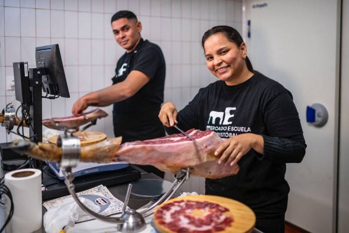 Dos trabajadores cortando jamón en un mostrador.