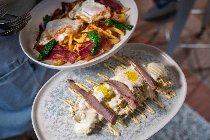 Un plato de ensaladilla y otro de huevos rotos con jamón.