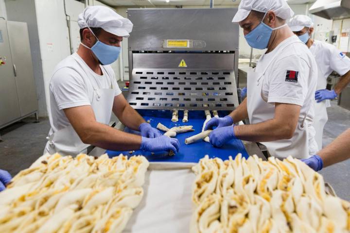 Dos trabajadores realizan a mano el trenzado de la trenza de Almudévar de la Pastelería Tolosana.