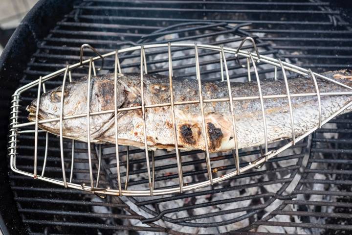 Una corvina mediana dentro de una besuguera sobre el fuego