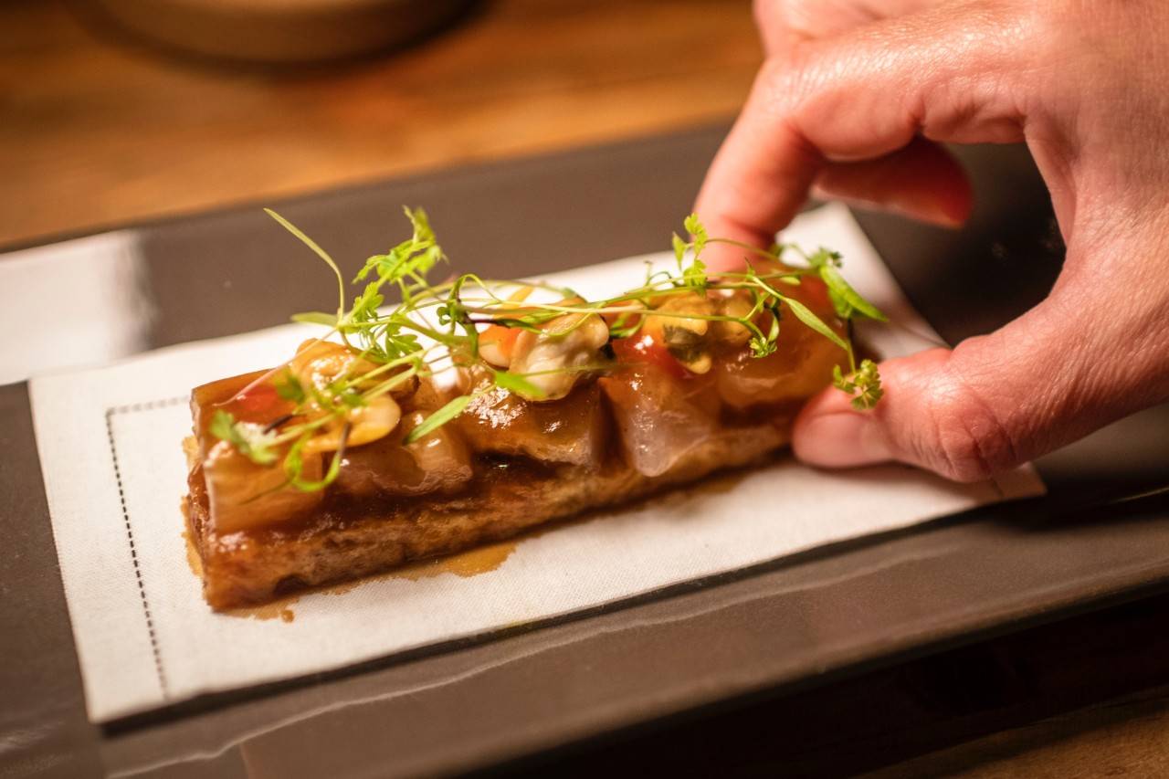 Focaccia de tendones de ternera, berberechos, mahonesa de lima y brotes.