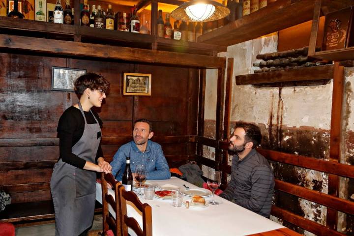 Una camarera atiende una de las mesas detrás de la que pueden verse las paredes descascarilladas por el humo.