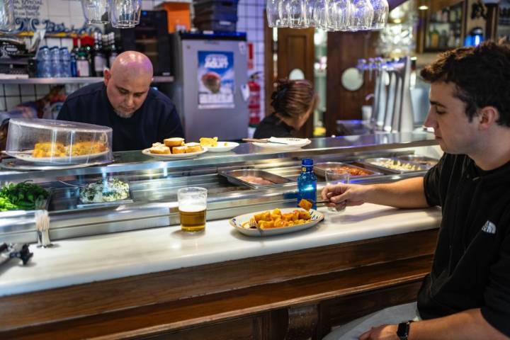 Chico comiendo patatas bravas en la barra del bar.