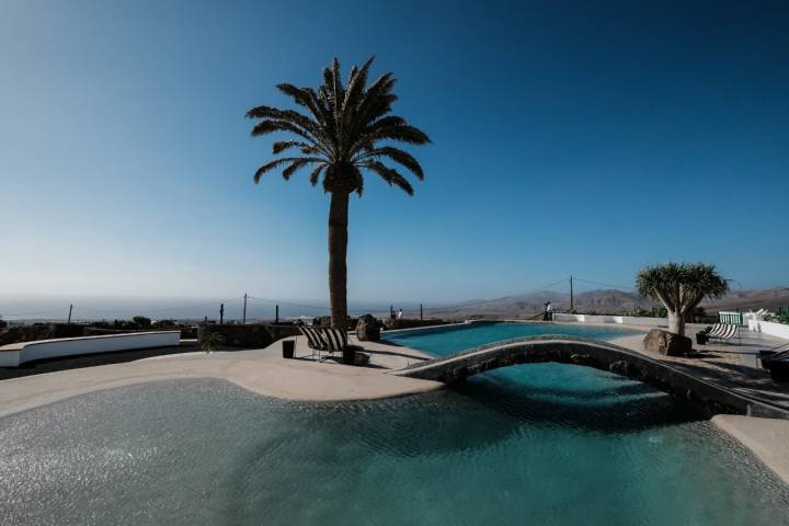 Vista parcial de la piscina con una palmera y los volcanes al fondo.