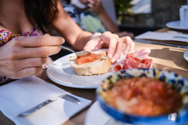 Las manos de una mujer preparan tomate con pan en la hora del desayuno.