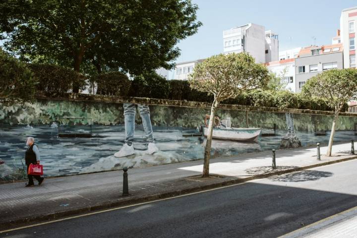 Una mujer pasea con su pantalla protectora ante el mural del río Eume, obra del colectivo Kasomiso.