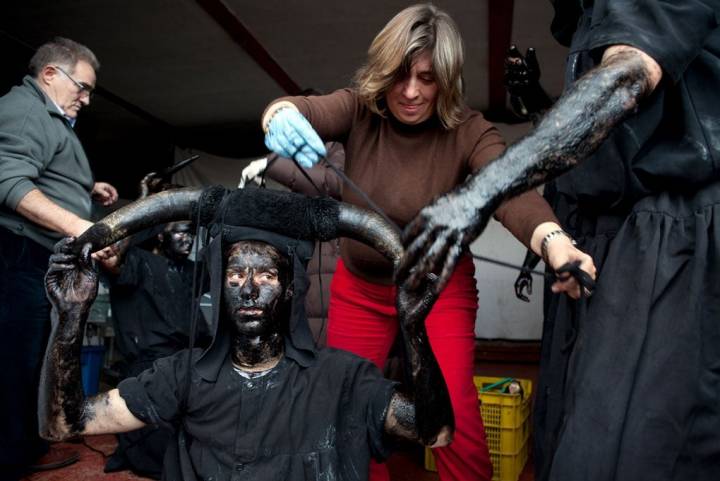 Una mujer ata a uno de los diablos los enormes cuernos de buey que lucen sobre sus cabezas.