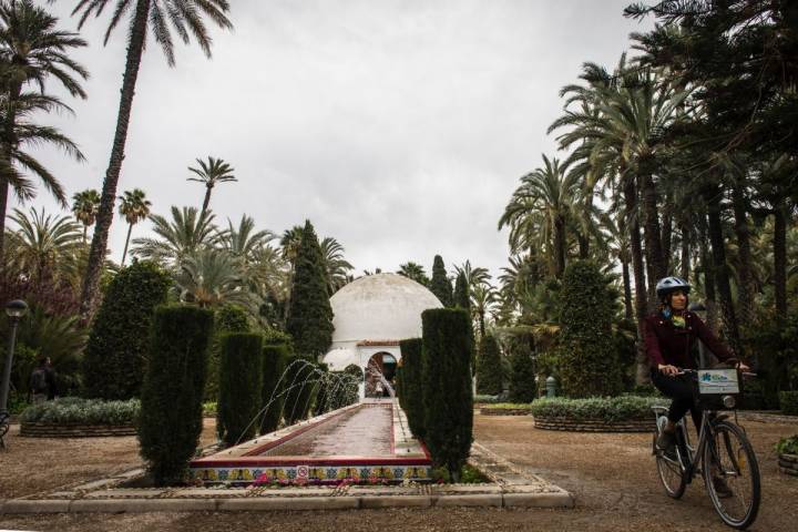 Pasando con la bici junto a una fuente del dentro de visitantes del parque municipal en Elche (Alicante).